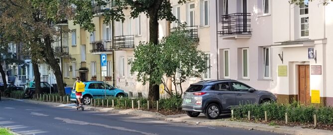 Drzewa obok jezdni na tle kamienicy.