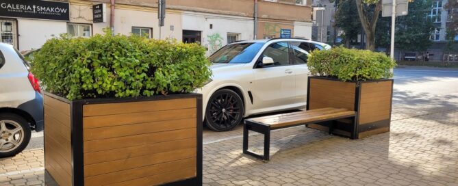 Ławka i dwie duże, drewniane donice z roślinnością.