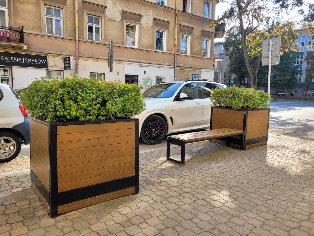Ławka i dwie duże, drewniane donice z roślinnością.