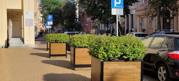 Chodnik, na którym stoją trzy duże, drewniane donice z roślinnością.