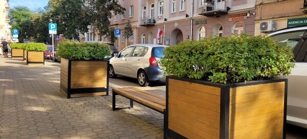 Ławka i dwie duże, drewniane donice z roślinnością.