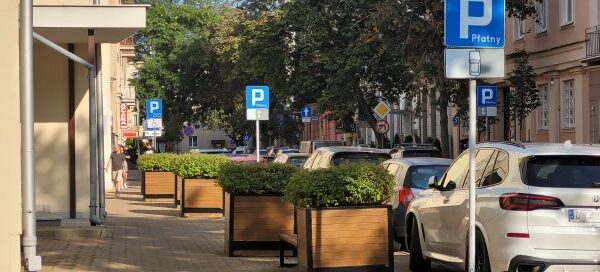 Chodnik, na którym stoją duże, drewniane donice z roślinnością.