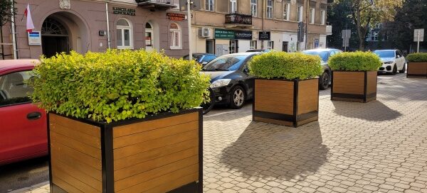 Chodnik, na którym stoją trzy duże, drewniane donice z roślinnością.