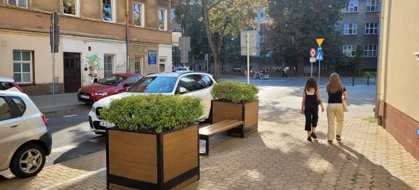 Ławka i dwie duże, drewniane donice z roślinnością.