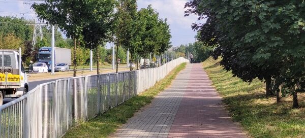 Ścieżka rowerowa oraz chodnik, oddzielone barierkami i trawnikiem od ulicy.