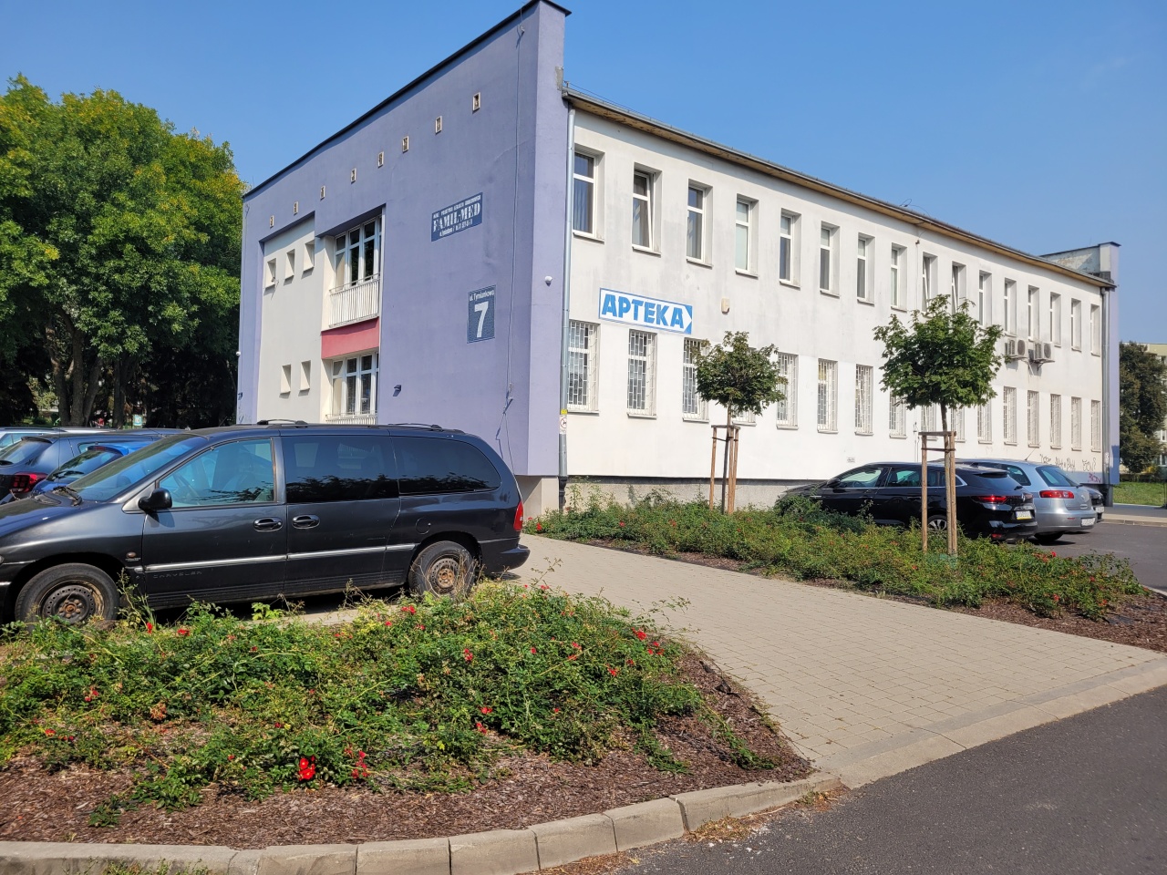 Trawniki przy parkingu. W tle widoczny budynek.