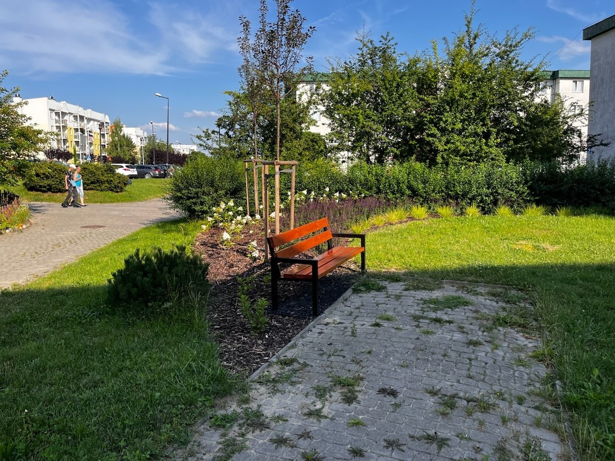 Zielony skwer na którym stoi ławka.
