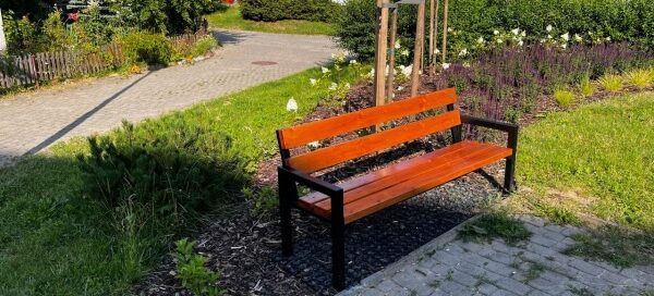 Zielony skwer na którym stoi ławka.