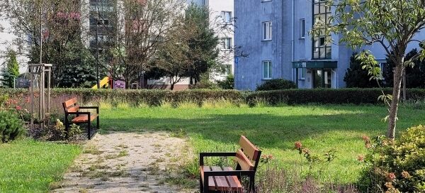 Zielony skwer na którym stoją ławki.