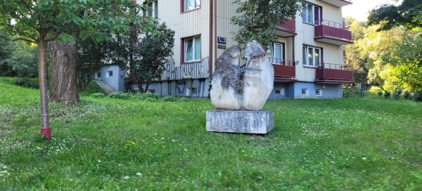 Rzeźba ustawiona na trawniku. W tle widać blok.