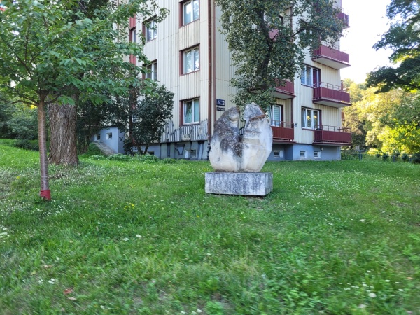 Rzeźba ustawiona na trawniku. W tle widać blok.