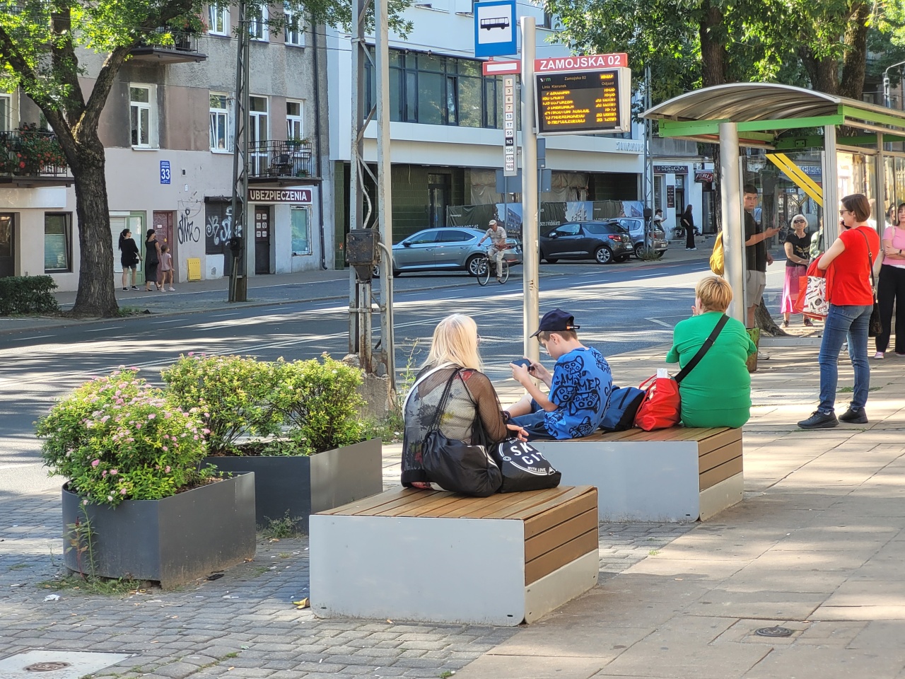 Ławki i donice z roślinnością, stojące obok przystanku autobusowego.