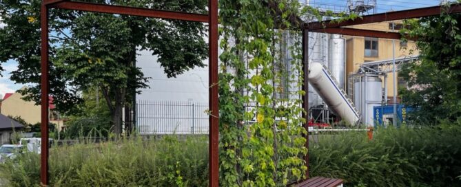 Mały skwer z ławkami i roślinnością na terenie obok fabryki.