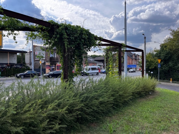 Mały skwer z ławkami i roślinnością na terenie obok fabryki.
