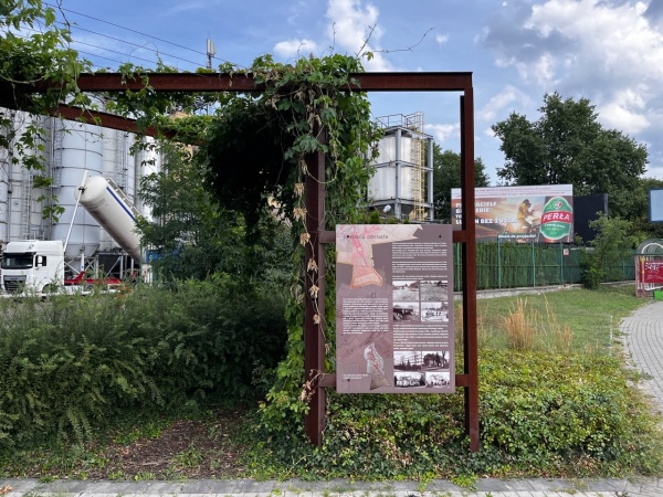 Mały skwer z ławkami i roślinnością na terenie obok fabryki.