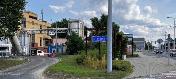 Mały skwer z ławkami i roślinnością na terenie obok fabryki.