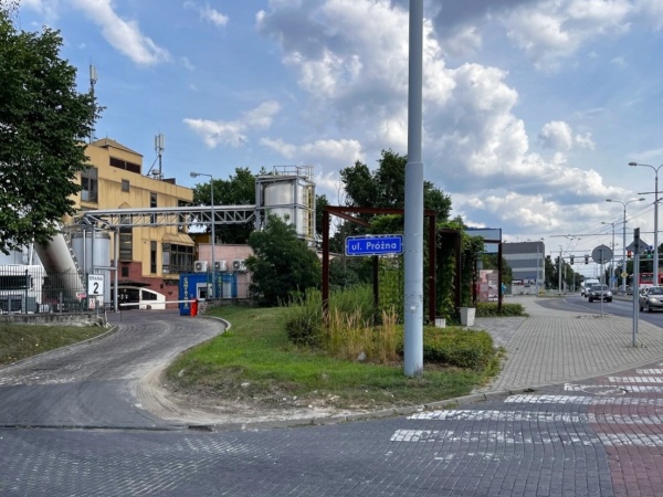 Mały skwer z ławkami i roślinnością na terenie obok fabryki.