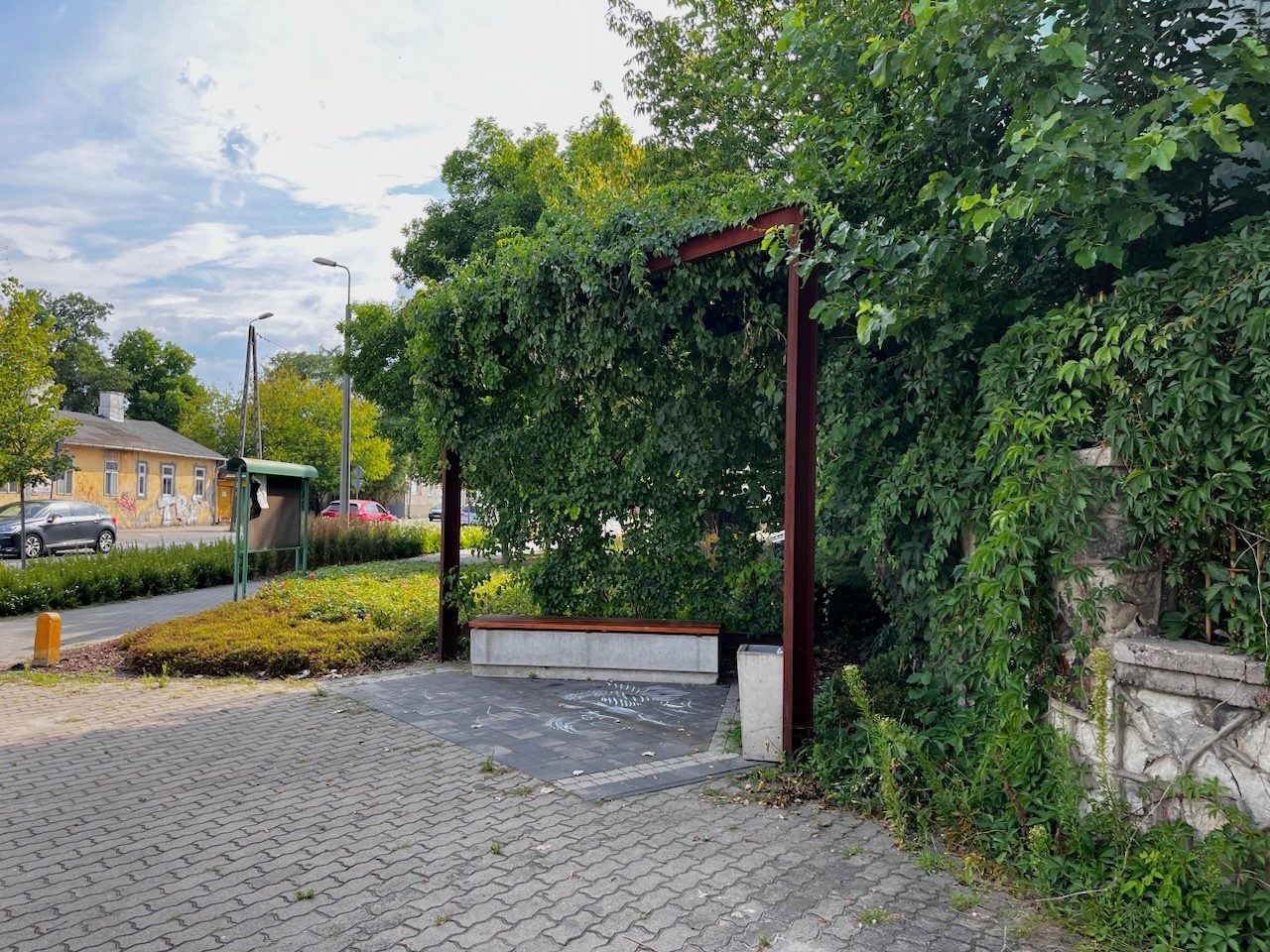 Mały skwer z ławkami, otoczony roślinnością.