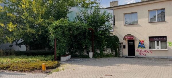 Mały skwer z ławkami, otoczony roślinnością.