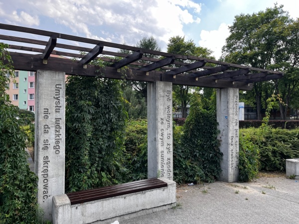 Miejsce odpoczynku na skwerze, otoczone roślinnością.