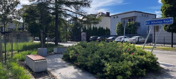Mały skwer z ławkami i zielenią, przy jednej z głównych ulic.