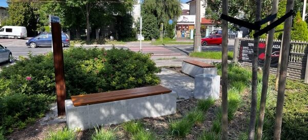 Mały skwer z ławkami i zielenią, przy jednej z głównych ulic.