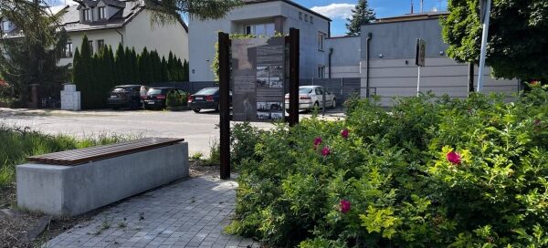 Mały skwer z ławkami i zielenią, przy jednej z głównych ulic.