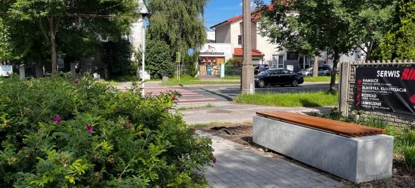 Mały skwer z ławkami i zielenią, przy jednej z głównych ulic.