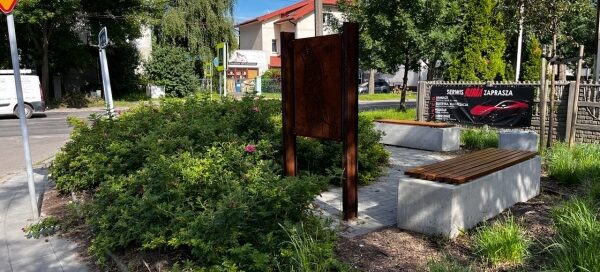 Mały skwer z ławkami i zielenią, przy jednej z głównych ulic.