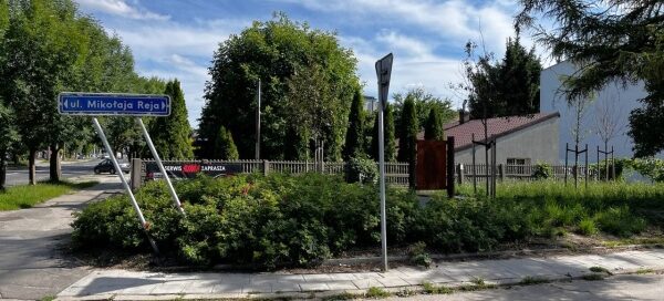 Mały skwer z ławkami i zielenią, przy jednej z głównych ulic.