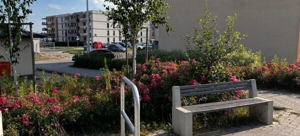 Stojak na rowery i betonowa ławka, ustawione na skwerze.