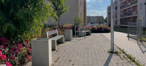 Betonowe kosze i ławki ustawione na skwerze.