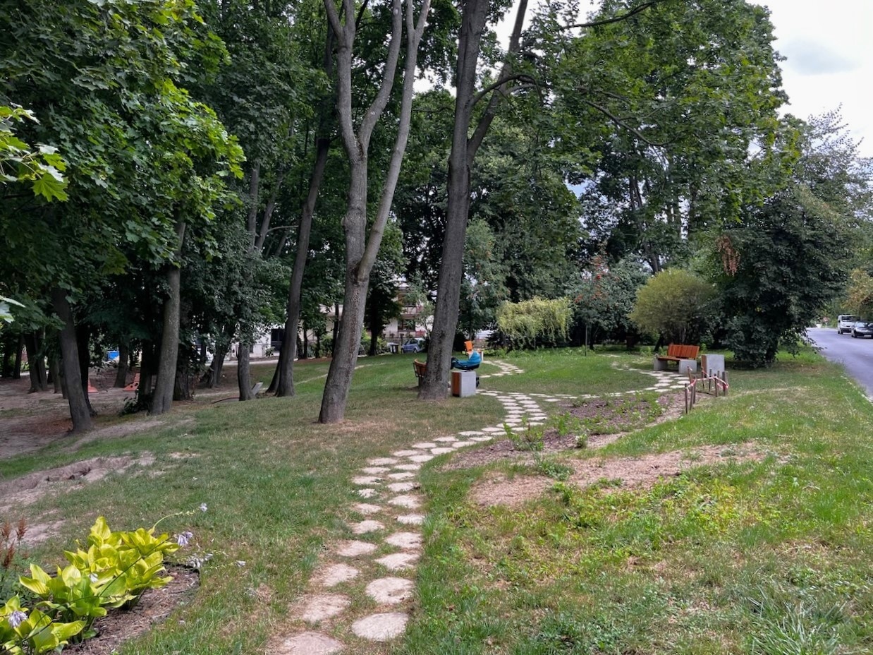 Ścieżka z nieregularnych płyt w trawniku, otoczona starodrzewami.