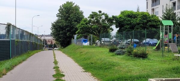 Ścieżka rowerowa i chodnik, pomiędzy ekranami akustycznymi a trawnikiem.