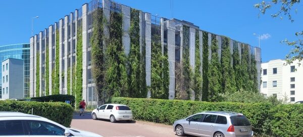 Wielopoziomowy parking, na ścianach którego, zasadzono pnącza. NA terenie wokół parkingu widoczny jest żywopłot.