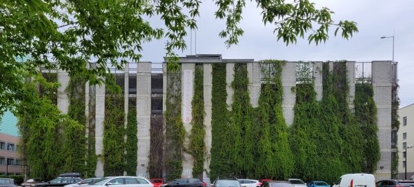 Wielopoziomowy parking, na ścianach którego, zasadzono pnącza. Teren przed parkingiem zdobi trawnik.