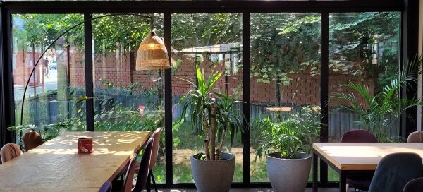 Widok z wnętrza restauracji, przez przeszkloną ścianę, na roślinność, na zewnątrz budynku.