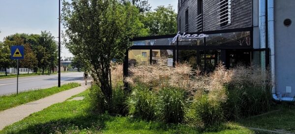 Teren przed restauracją z trawnikiem i nasadzeniami roślinnymi.