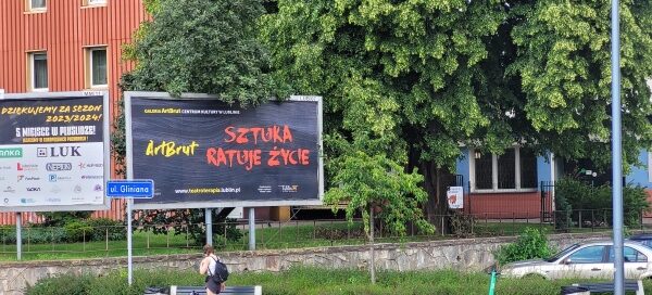 Mały skwer z nasadzeniami roślinnymi, ławką i koszem.