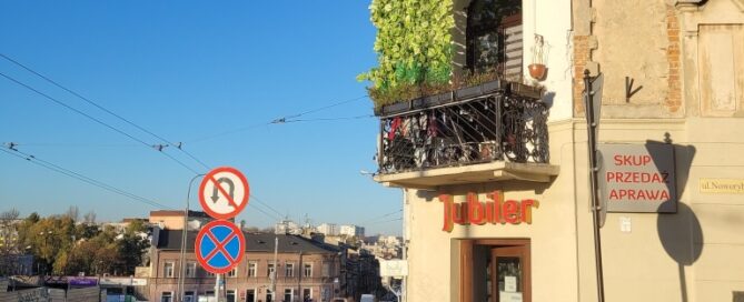 Balkon ozdobiony sztucznymi pnączami, usytuowany na rogu kamienicy.