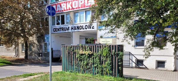 Pnącza oplatające ściany paczkomatu. W tle widoczny budynek.