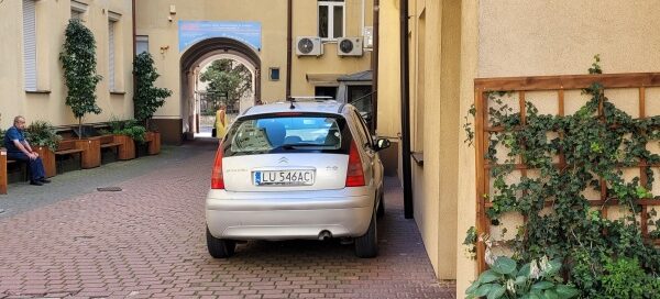 Drewniane ławki i donice z roślinnością, ustawione na podwórzu kamienic.