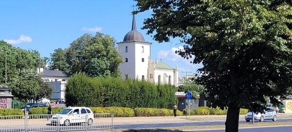 Jezdnia oddzielona pasem zieleni z nasadzeniami krzewów i drzew. W tle widoczna jest cerkiew.