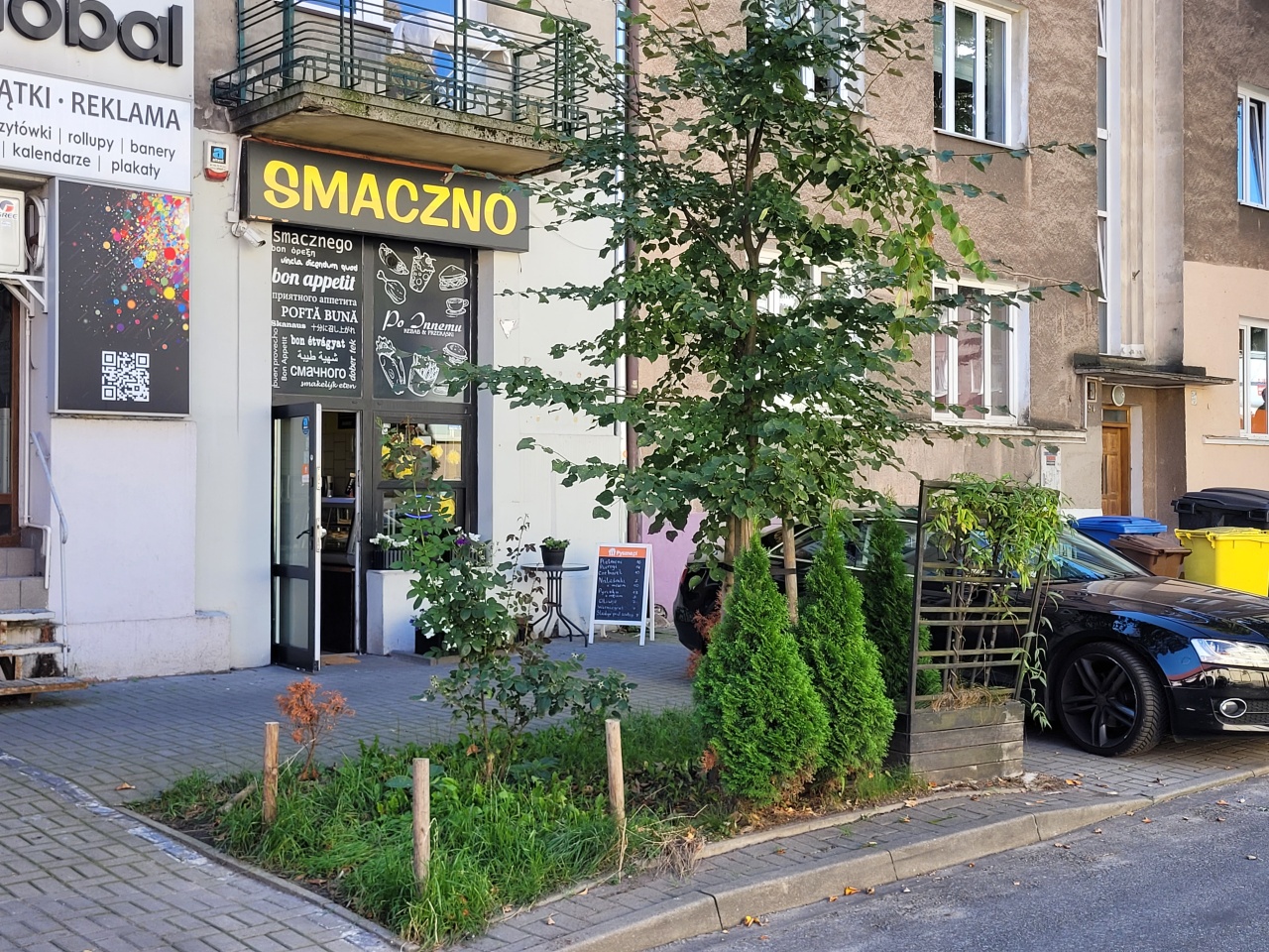 Teren trawnika z nasadzeniami roślinnymi przed lokalem usługowym.