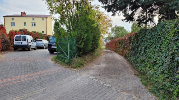 LacznikWillowejiSlawinka4 Prywatna posesja z budynkiem mieszkalnym. Obok niej widoczna droga gruntowa po obu stronach otoczona ogrodzeniem, na którym zasadzono pnącza.