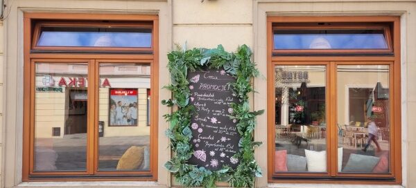 Menu wiszące przed jednym z lokali, ozdobione zieloną roślinnością.