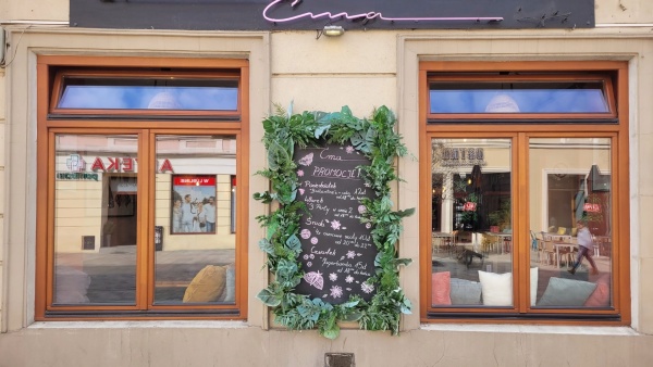 Menu wiszące przed jednym z lokali, ozdobione zieloną roślinnością.