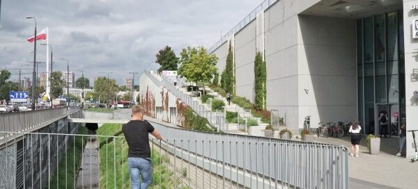 Budynek galerii handlowej. W nowoczesną bryłę budynku wkomponowana jest roślinnoś. Pnącza, drzewa i nasadzenia roślinne ozdabiają cały budynek.