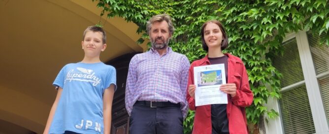 Trzy osoby stojące w podwórzu kamienic. Ściany budynku w tle, porośnięte pnączami.